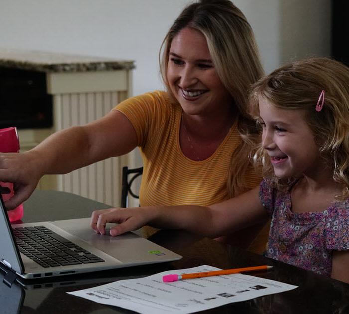 一位母亲和她的女儿在网上上课时指着笔记本电脑屏幕