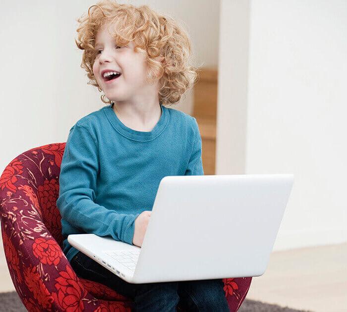 一个年轻的白人男孩坐在椅子上，手里拿着笔记本电脑