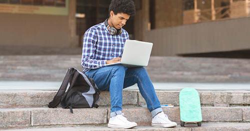 An online student sitting on steps outside while researching college websites for high school students on a laptop.